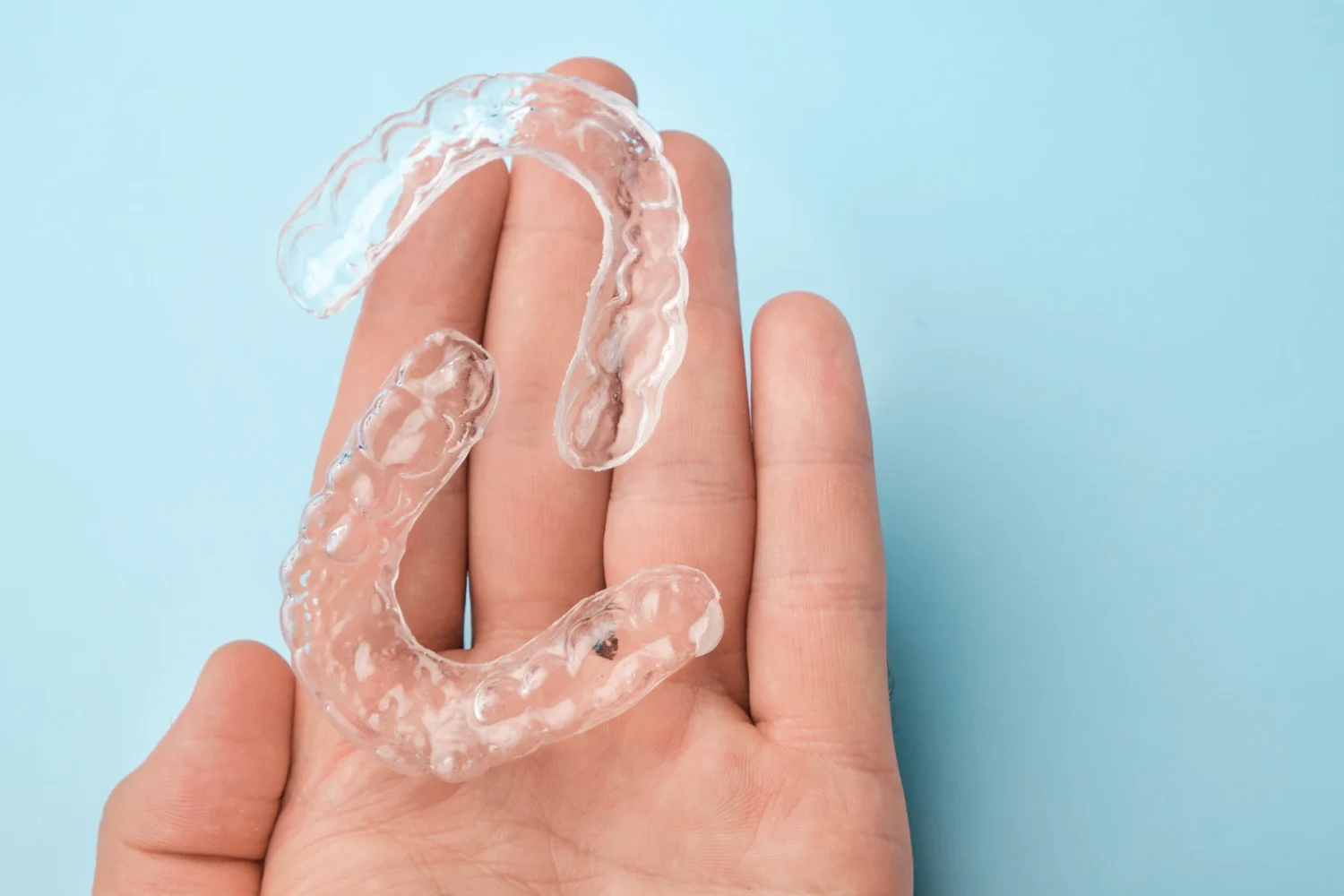 Hand holding clear aligners with a light blue background